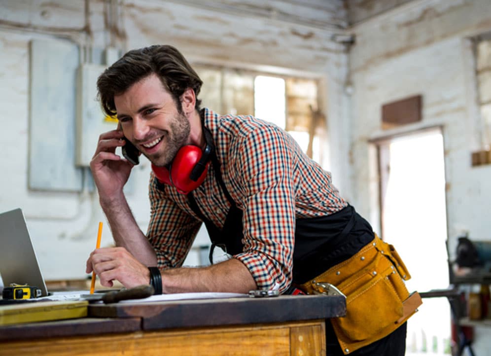 Carpenter on phone with client leaning over worktable