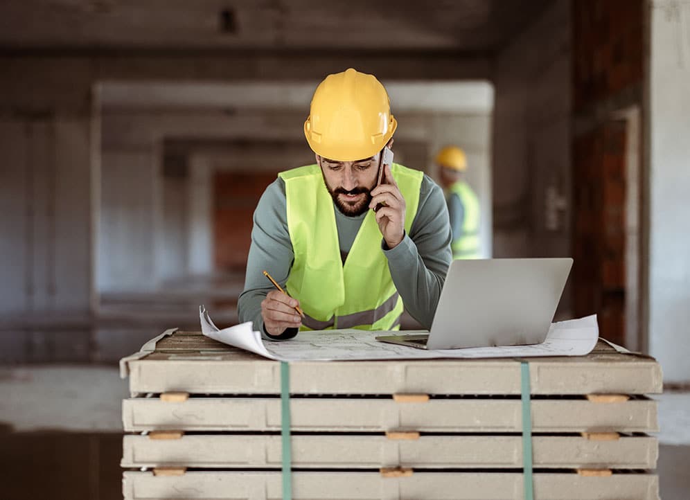 Construction worker talking to client on phone and leaning over box with laptop 2