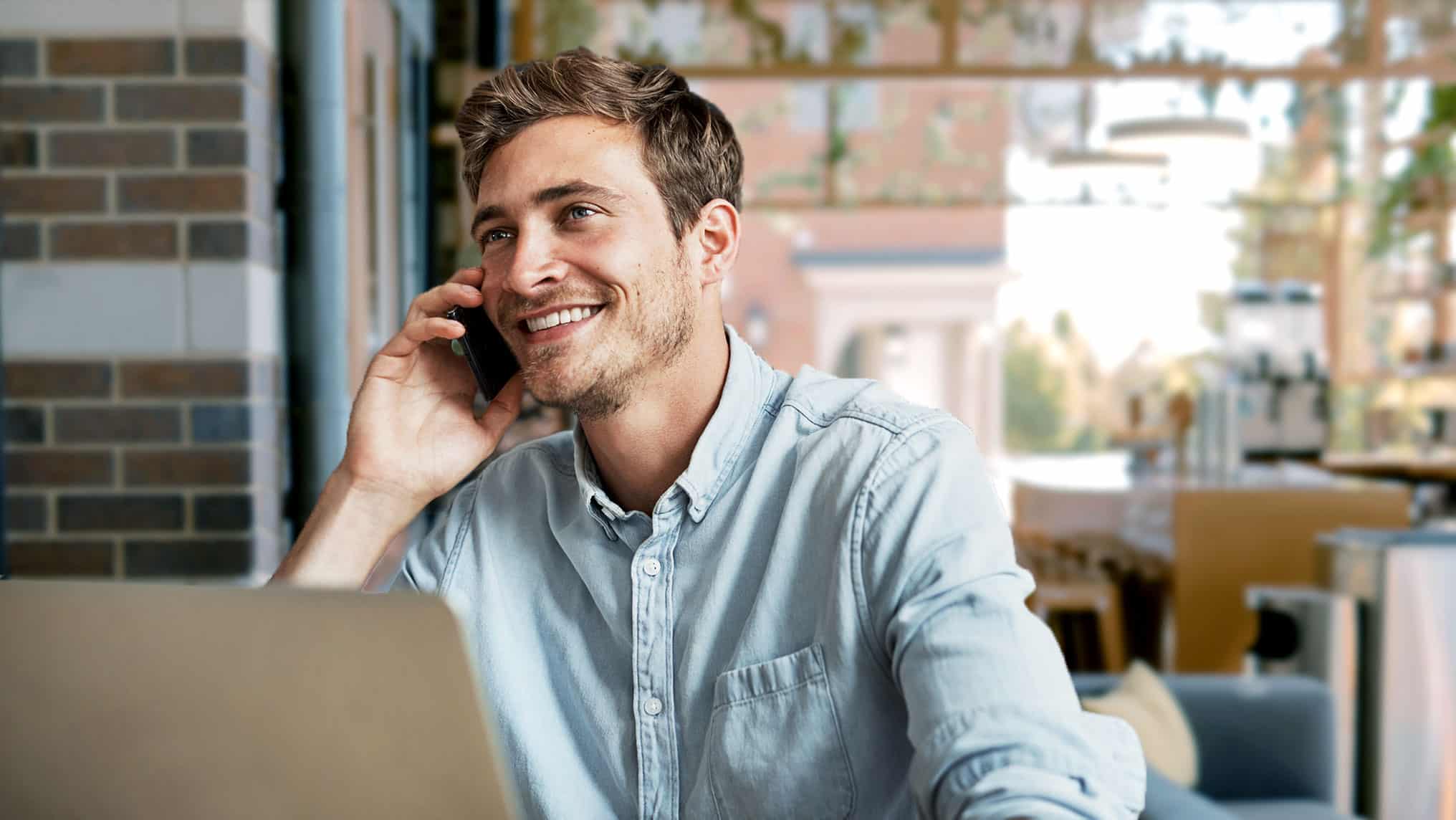 Man calling business associate while working with laptop in cafe