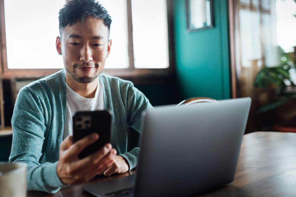 Man working in cafe with mobile phone and laptop