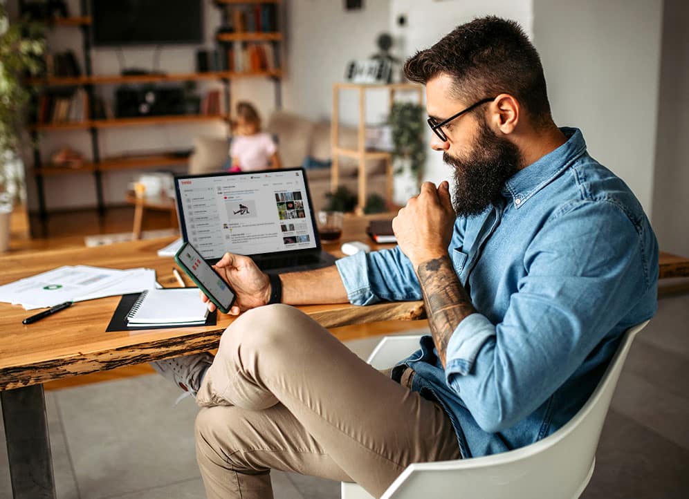 Man looking at phone with laptop on desk